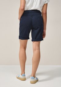 Marineblauwe shorts met omgestikte zoom, meerdere zakken en een gestructureerde tailleband, gecombineerd met witte sneakers met blauwe accenten.