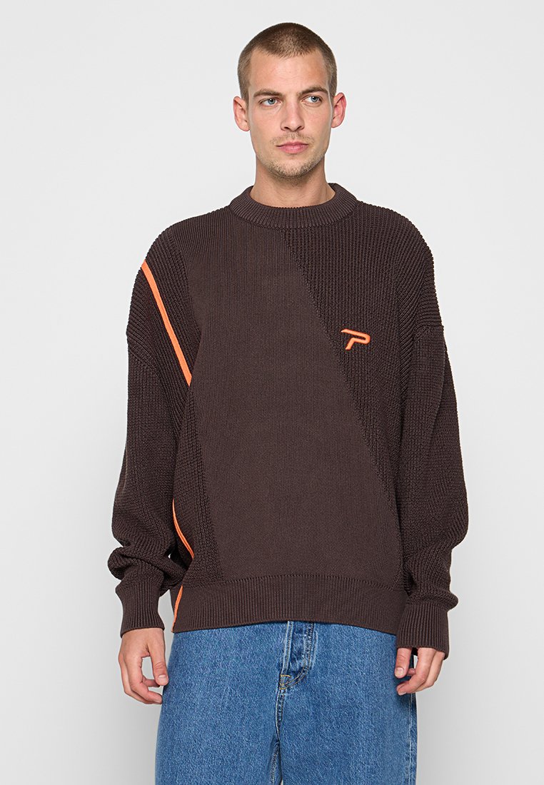 Pull en tricot marron foncé avec un motif diagonal, une bande d'accent orange et un petit logo sur la poitrine. Coupe décontractée.