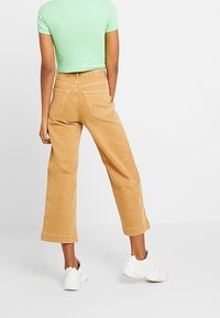 Tan wijdvallende corduroy broeken met een cropped lengte, achterzakken en een gladde textuur, gecombineerd met een lichtgroen geribd shirt en witte sneakers.