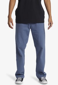 Light blue, straight-leg pants made of cotton with a smooth texture; worn with a black shirt and black-and-white sneakers.