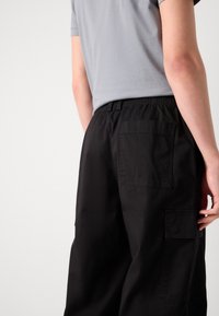 Pantalons cargo noirs avec une taille élastique, dotés de poches arrière et d'une coupe décontractée. Le tissu semble lisse avec une texture minimale.
