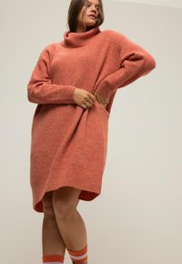 Abito maglione a collo alto oversize in un colore pesca testurizzato, con polsini a coste e orlo arrotondato, abbinato a calze a righe.