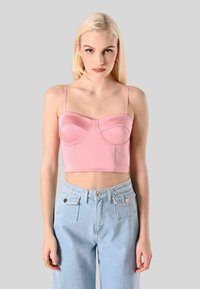 Top corto rosa con coppe strutturate, spalline sottili, tessuto liscio. Abbinato a jeans in denim azzurro chiaro a vita alta con tasche frontali.