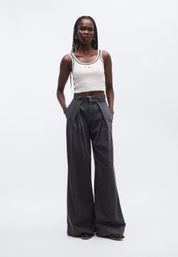 Bílý pletený crop top s černým obtahem, v kombinaci s vysokým pasem, širokými kalhotami tmavě šedé barvy s opaskem a bočními kapsami.