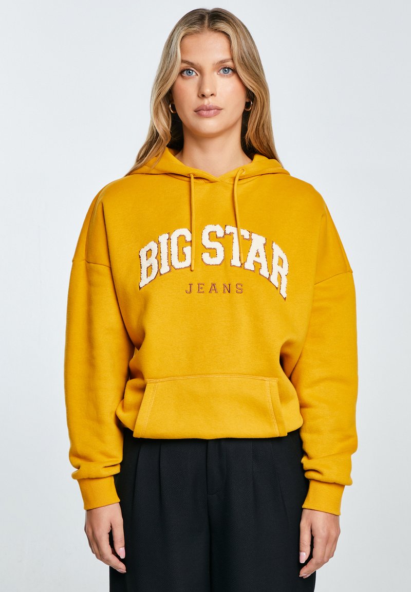 Żółta bluza z kapturem z białym haftem "BIG STAR JEANS". Posiada kieszeń z przodu oraz ribbowe mankiety, wykonana z miękkiego materiału.