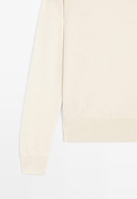 Sweter w kolorze kremowym z prążkowanymi mankietami i dolnym wykończeniem, charakteryzujący się miękką teksturą i luźnym krojem. Brak widocznych wzorów lub elementów metalowych.