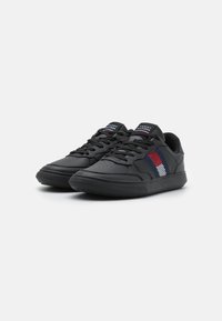 Sneaker atletici neri realizzati in pelle sintetica, con suola testurizzata, punta forata e un design a tre colori in rosso, bianco e blu.