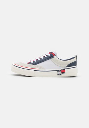 Sneakers con una combinazione di materiali superiori bianchi, grigi e blu navy, con accenti rossi e blu, pannelli testurizzati e un dettaglio del logo in evidenza.