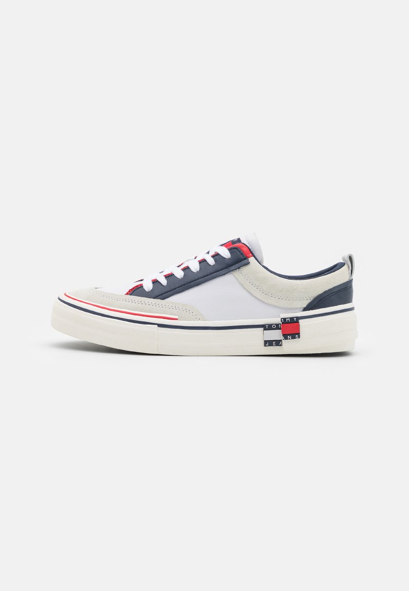 Sneakers con una combinazione di materiali superiori bianchi, grigi e blu navy, con accenti rossi e blu, pannelli testurizzati e un dettaglio del logo in evidenza.