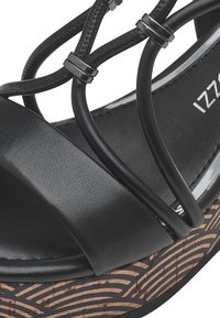 Black platform sandal featuring a smooth synthetic upper, crisscross straps, metallic accents, and a textured, patterned cork-like sole.