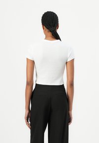 Polo shirt blanc raccourci à manches courtes, avec un col classique et une texture lisse, associé à un pantalon noir taille haute.