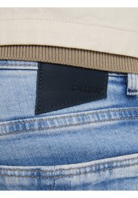 Jeans med en ljusblå tvätt, med en mörk läderlapp märkt "CHASIN'" nära midjan, sydda fickor och en tygtop.