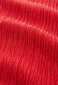 Tissu texturé rouge avec un motif en ondulation, mettant en valeur une texture douce et fibreuse ainsi que des nuances de rouge variées, créant ainsi de la profondeur et un intérêt visuel.