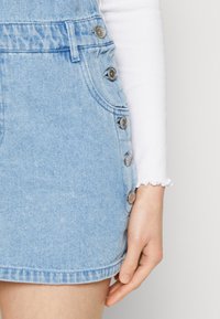 Vaaleansininen denimpitkä hame, jossa on hopeiset napit sivussa, frayed-helma ja joka on yhdistetty valkoiseen pitkähiharaiseen paitaan.