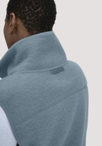 Blauer Fleece-Weste mit hohem Kragen, ausgestattet mit einer strukturierten Oberfläche und dezentem Logodruck. Glatte Nähte und minimalistische Designelemente.