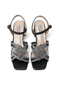 Sandali neri con tacco a spillo e punta quadrata, caratterizzati da un intricato design a croce con accenti metallici e una superficie testurizzata.