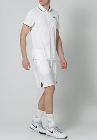 Biała koszulka polo z czarnymi i zielonymi akcentami, w zestawieniu z pasującymi białymi szortami. W połączeniu z białymi butami Nike i skarpetkami, podkreślającymi sportowy styl.