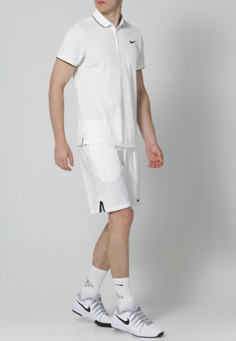 Biała koszulka polo z czarnymi i zielonymi akcentami, w zestawieniu z pasującymi białymi szortami. W połączeniu z białymi butami Nike i skarpetkami, podkreślającymi sportowy styl.