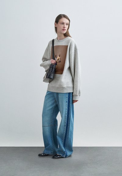 Felpa grigia con una grande stampa grafica, abbinata a jeans blu a gamba larga con una banda laterale. A completare il look, una piccola borsa nera.