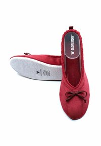 Ballerine en suede rouge avec un bout rond, détail de nœud décoratif et semelle en caoutchouc blanc texturé. Logo visible sur la semelle intérieure.