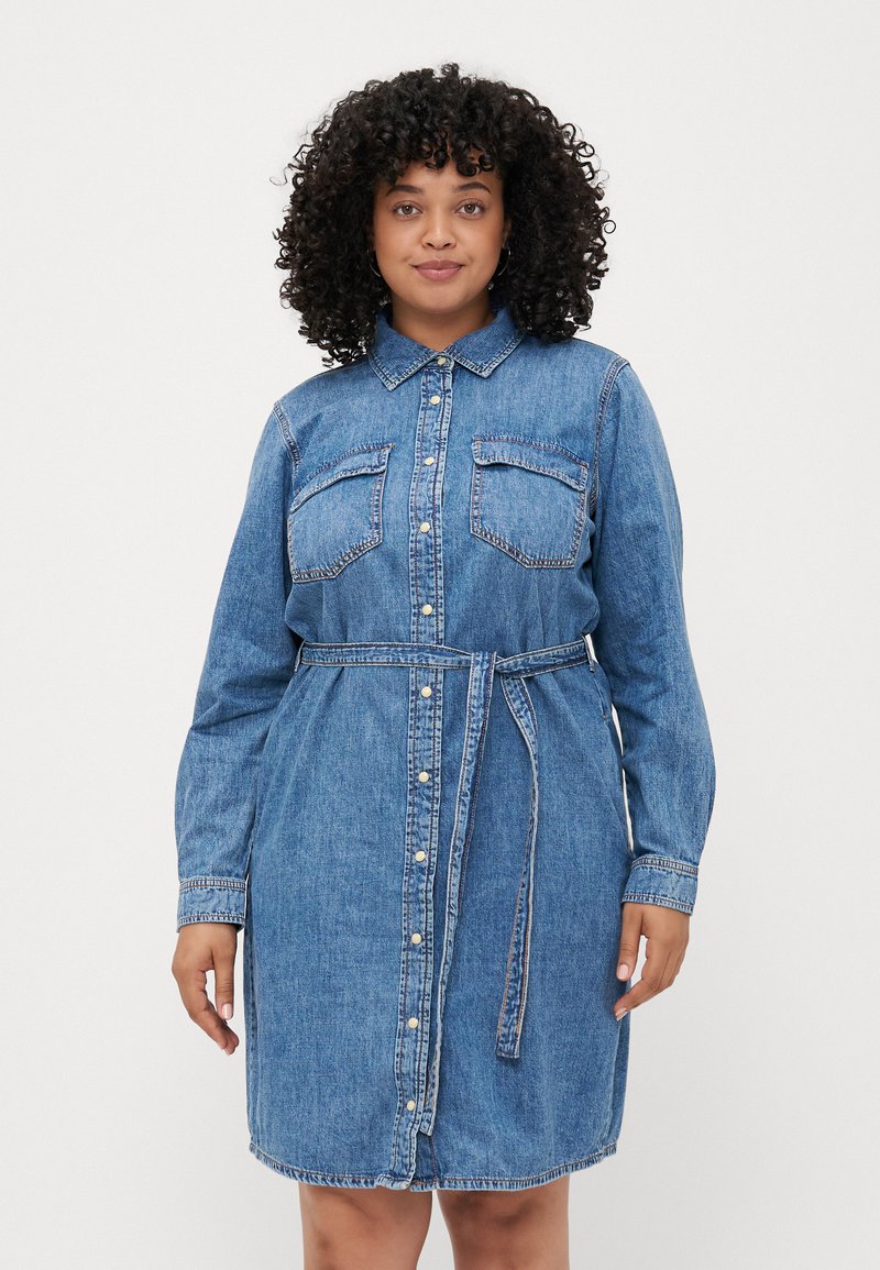 Denim skjortekjole, lett falmet blå, lange ermer, knapping foran, to brystlommer, belte i midjen og sømdetaljer.