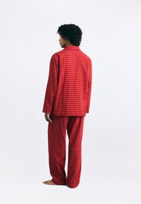 Red checkered pajama set features long sleeves and loose-fitting pants, made of soft fabric. Visible square pattern, minimal design.