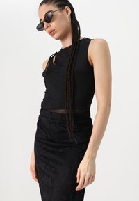 Must have mustrõhuga must sans sleeveless topp, millel on läbipaistev detail, kombineeritud sobituvate mustade seelikutega, millel on keerukad lillemustrid. Kanna ovaalseid prille.