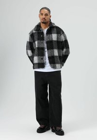 Zwart-grijs geruite fleece jas met een kraag, knoopsluiting, gecombineerd met zwarte jeans met wijde pijpen en zwarte veter schoenen.