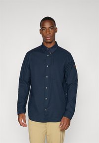 Camicia blu marina con colletto e maniche lunghe, dotata di bottoni metallici e una tasca sul petto. Tessuto con una texture liscia.