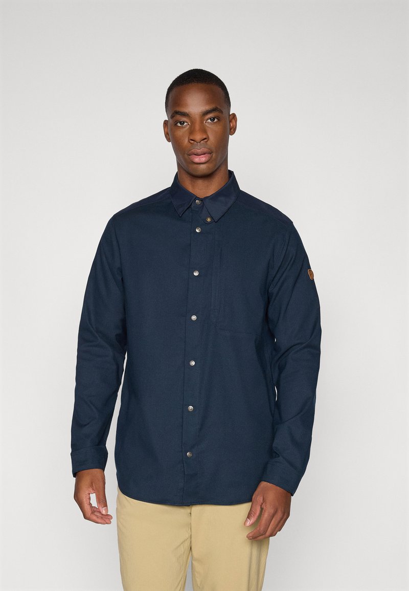 Camicia blu marina con colletto e maniche lunghe, dotata di bottoni metallici e una tasca sul petto. Tessuto con una texture liscia.
