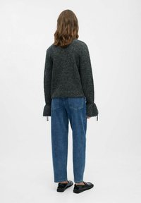 Grå strikket sweater med brede ærmer, parret med blå denim jeans. Bemærkelsesværdige snore ved ærmeenderne og afslappede sorte sko.
