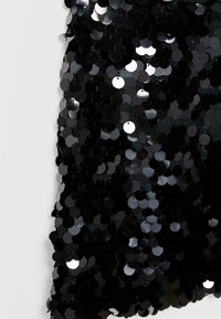 Tessuto nero ricoperto densamente di paillettes nere rotonde e brillanti che riflettono la luce su uno sfondo bianco semplice.