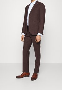 Costume marron texturé à la coupe ajustée, associé à une chemise bleu clair et des chaussures habillées en cuir marron brillant.