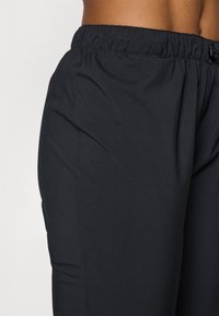 Black athletic pants with an elastic waistband, smooth texture, and a fitted design. They feature side seams for a streamlined look.