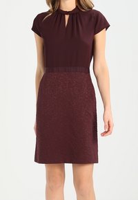 Burgundy dress with short sleeves, keyhole neckline, textured lower half, solid waistband, and a tailored fit. Smooth fabric throughout.