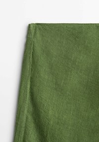 Tissu en lin vert avec une surface texturée, présentant un ourlet propre le long d'un bord, mettant en valeur une teinte naturelle et discrète.