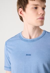 T-shirt de algodão azul claro com decote redondo, apresentando um discreto logótipo "BOSS" em azul mais escuro no peito e uma textura suave.