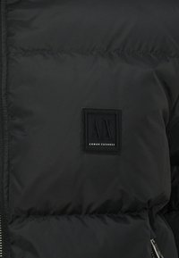 Schwarze Daunenjacke mit elegantem Finish, horizontaler Steppung und einem quadratischen bestickten Logo-Patch mit der Aufschrift "Armani Exchange".