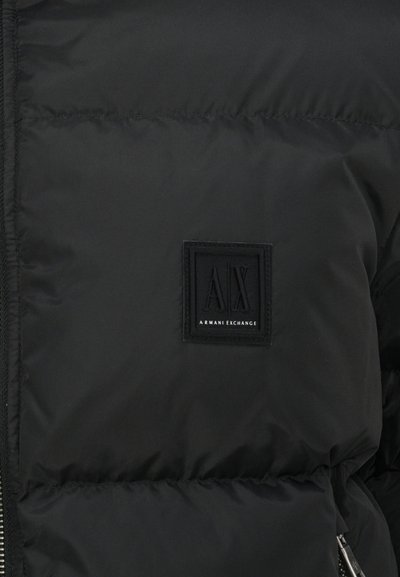 Doudoune noire à texture matelassée, avec une étiquette carrée noire portant l'inscription "AX" et "ARMANI EXCHANGE" en lettres blanches.