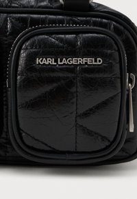 Mazs melns quiltēts ādas maciņš ar sudraba "KARL LAGERFELD" logotipu un rāvējslēdzēja vilkšanas cilpu labajā pusē.
