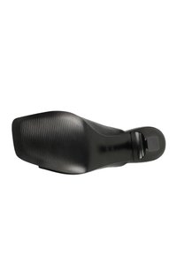 Semelle de chaussure habillée noire à bout carré, avant texturé pour l’adhérence et petit talon avec pièce de talon visible sur fond blanc.