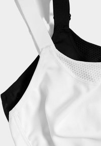 Svart och vit sport-bh med slät tyg, mesh-detaljer på den vita sidan, breda band och kontrasterande färger för design.
