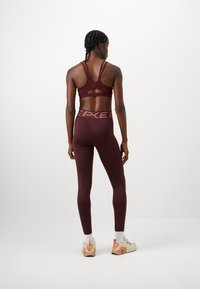 Soutien-gorge de sport bordeaux avec un design à bretelles et des découpes, associé à un legging taille haute assorti avec une ceinture logo rose.