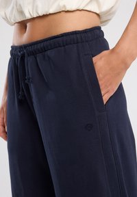 Donkerblauwe sweatpants met een elastische tailleband, zijzakken en een logo-applicatie. Gemaakt van zachte stof met een relaxte pasvorm.