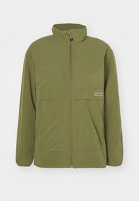 Veste zippée vert olive avec col montant, poignets élastiques, poches avant et petite étiquette de marque sur la poitrine.