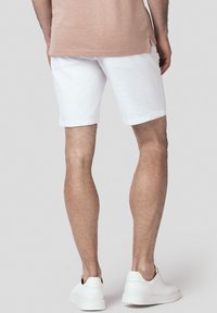 Białe bawełniane szorty o luźnym kroju, kończące się tuż nad kolanem. Noszone z jasnoróżową koszulką i białymi sneakersami.