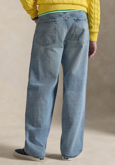 Modre kavbojke z visokim pasom in sproščenim krojem, z dvema zadnjima žepoma in rahlim bledenjem. Kombinirane z rumenim puloverjem z vzorcem kit.