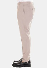 Pantaloni beige su misura in tessuto liscio, con tasche laterali e una tasca posteriore, abbinati a scarpe nere slip-on.