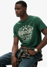 Grøn bomulds t-shirt med et fremtrædende hvidt grafisk design, parret med blå denim jeans og et ternet flannel skjorte bundet om livet.