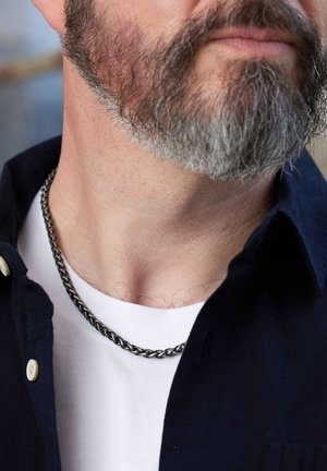 Silver chain necklace featuring a twisted design, worn over a white T-shirt, with a dark shirt visible at the collar.